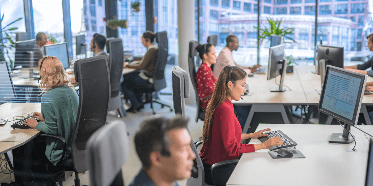 An office with 10 or more service desk employees working at their computers with headsets on.