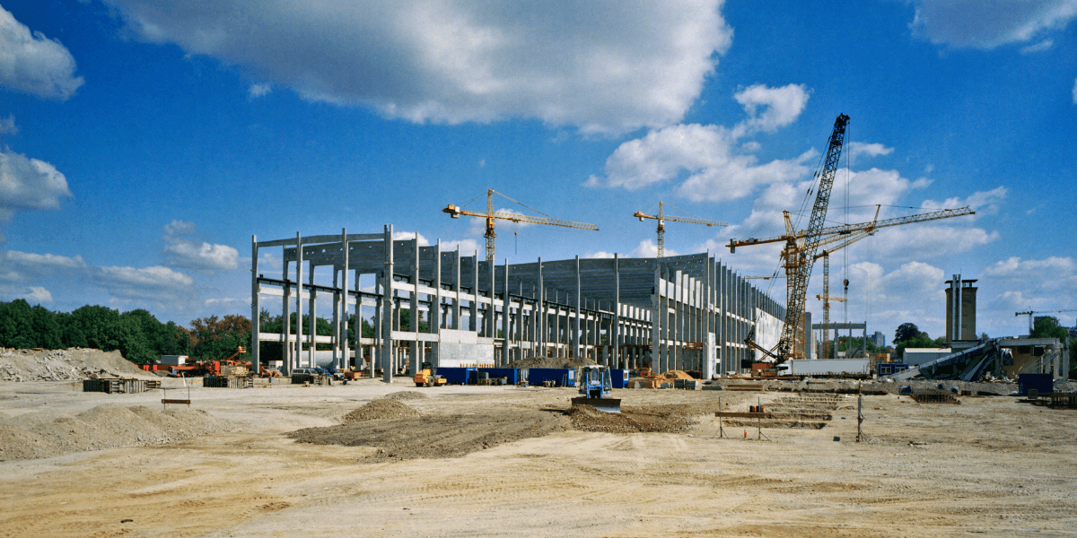 Industrial construction project featuring steel structural framework, tower cranes, and active commercial building development site.