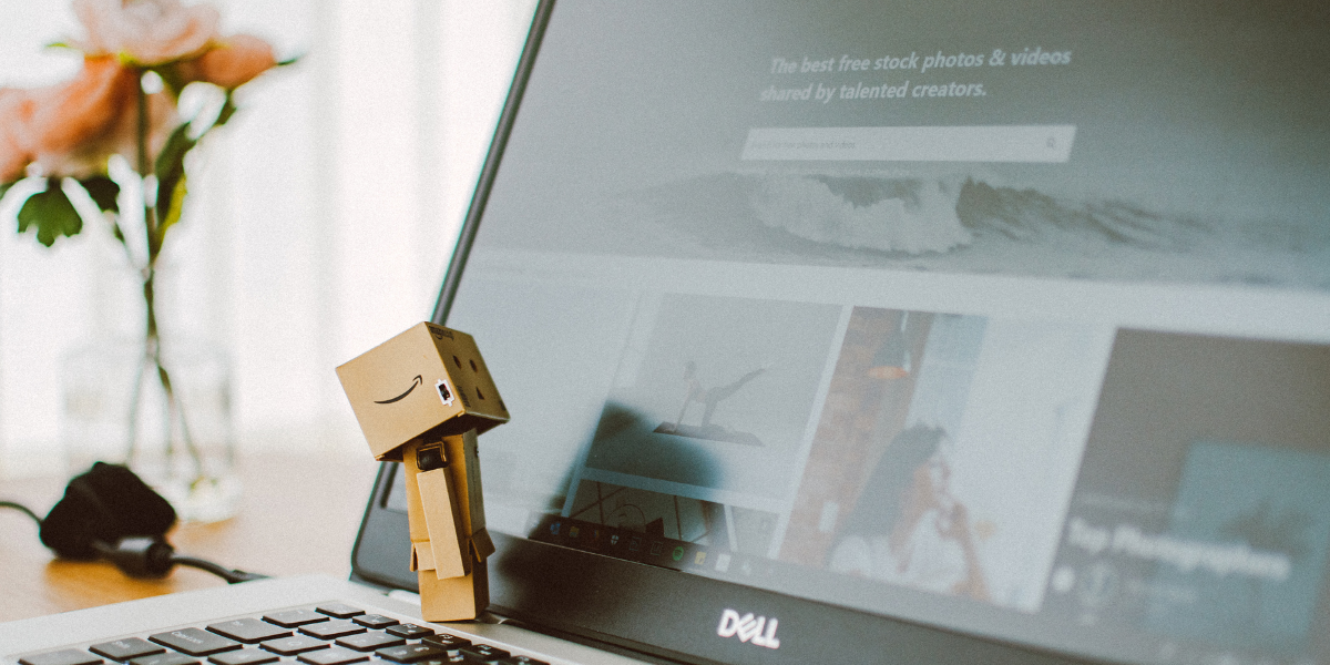 An Amazon-branded cardboard figure leaning against a Dell laptop displaying a webpage, symbolizing the connection between e-commerce and digital strategy.