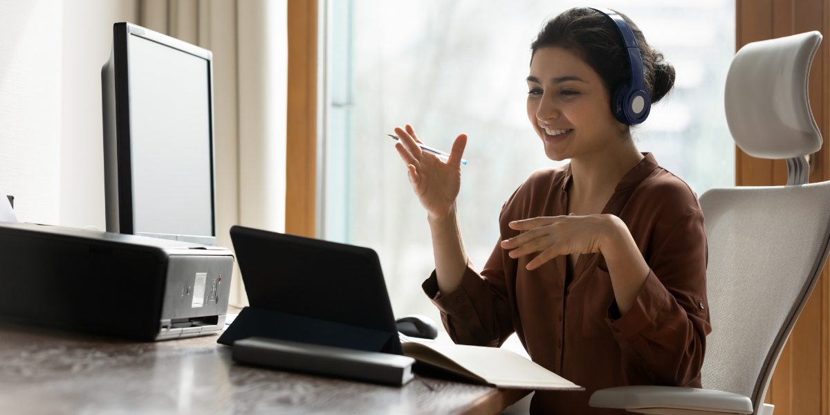 Customer service representative with headphones on a call with laptop and desktop in front of her