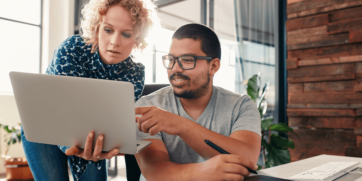 Two colleagues collaborating while reviewing content on a laptop, representing teamwork and marketing strategy planning.