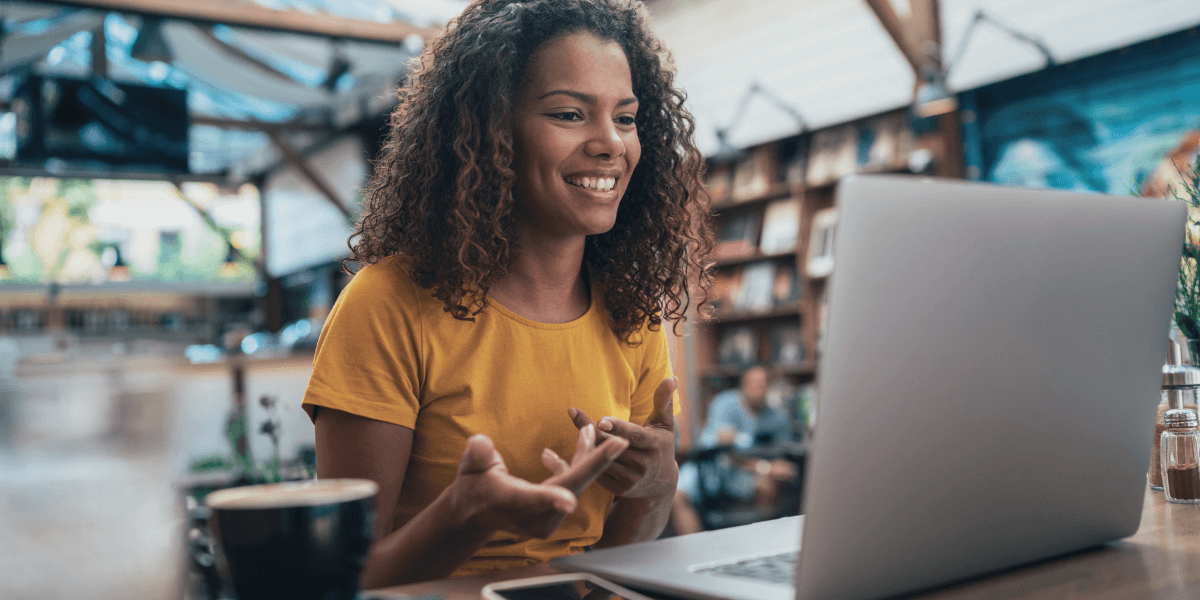 Young woman in a café smiling during a video call on her laptop, representing personalized video communication with Vidyard.