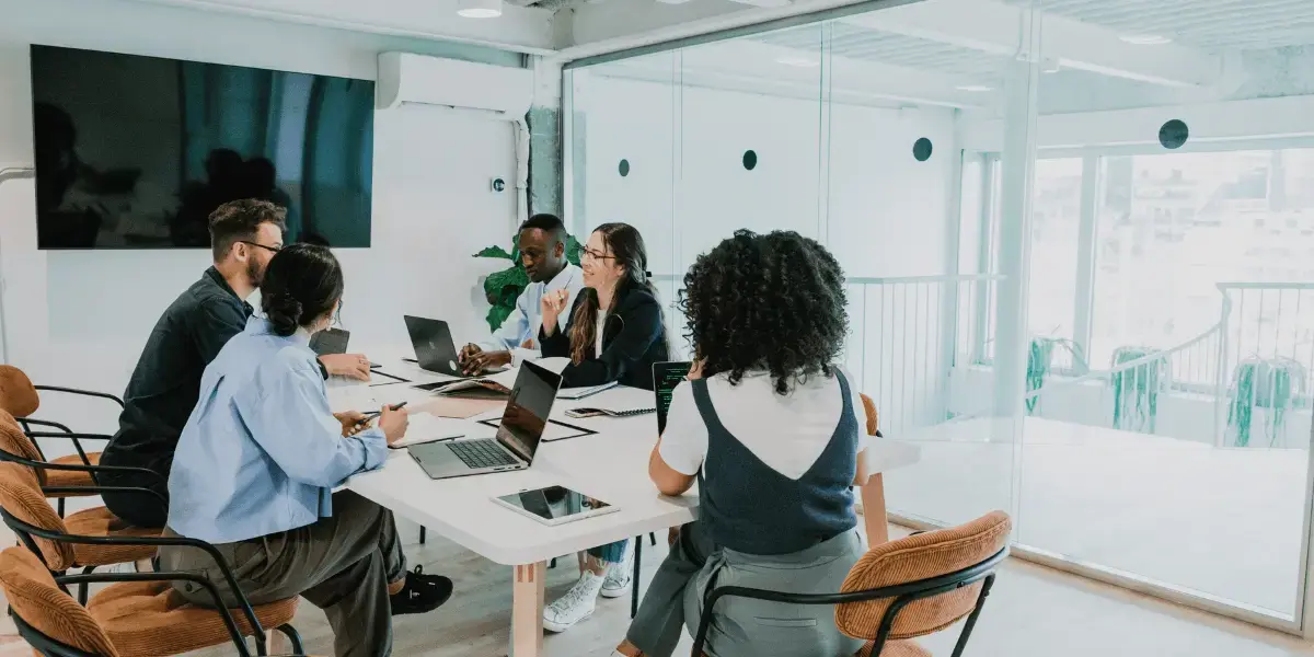 A group of people sitting around a table in a glass wall conference room