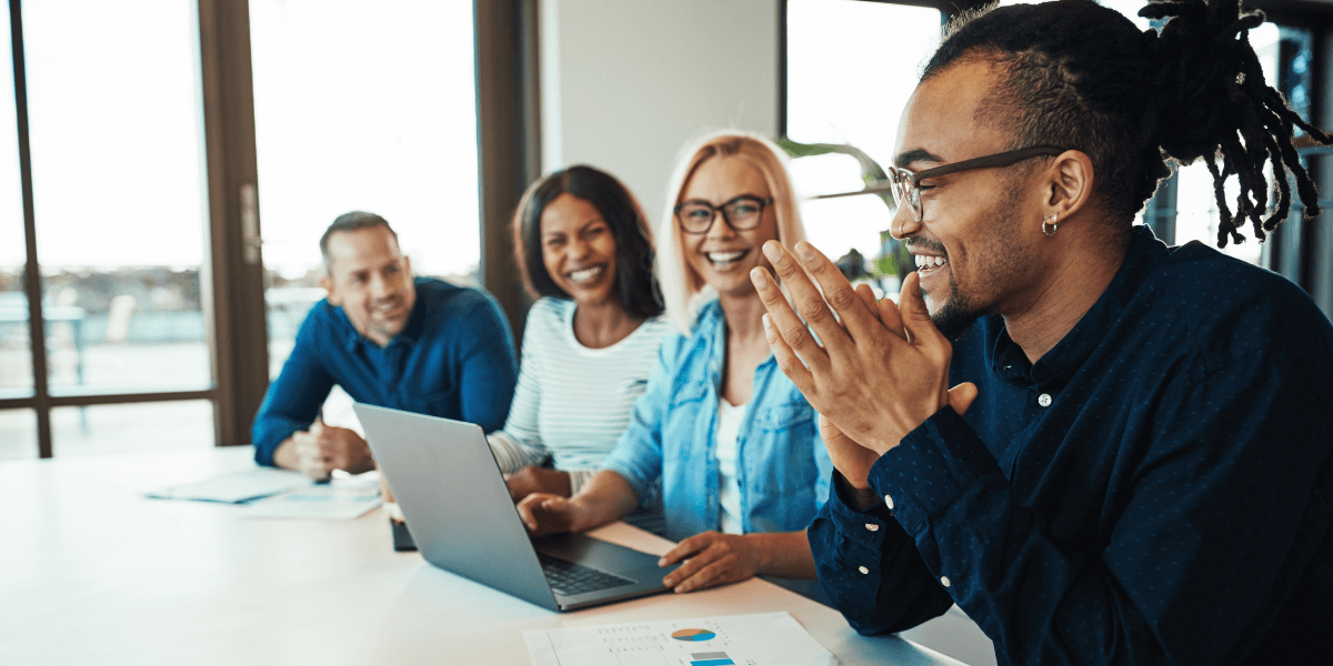A group of workers sitting around a table in an office looking at a laptop to learn lead generation tips and tricks.