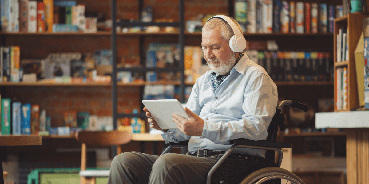 Older gentleman in a wheelchair with headphones, using a tablet.