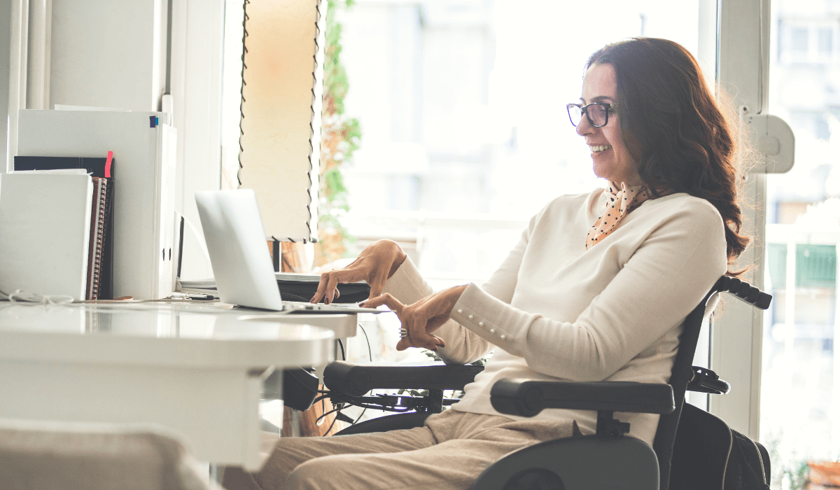 Woman in a wheelchair with a muscular disability at a desk using a laptop | Vested Feature image for Blog titled What is ADA Compliance?